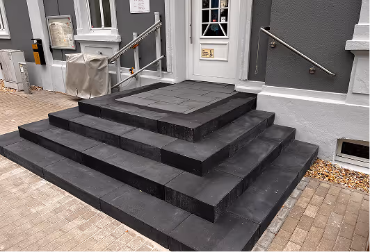 Schwarze Stufen mit Geländern führen zu einem weißen Haus- oder Geschäftseingang mit grauen Wänden.