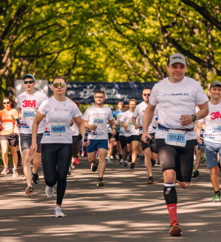 Group of runners participating in a race on a tree-lined path, wearing numbered race bibs and athletic gear.