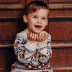 Smiling young boy wearing a patterned sweater seated in front of wooden paneling.