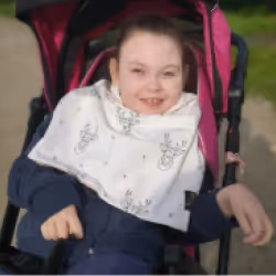 Smiling young person sitting in a pink stroller outside on a sunny day.