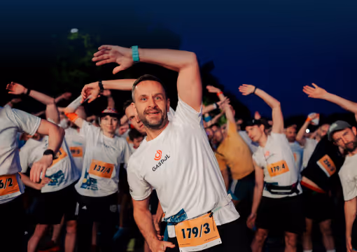 Group of runners stretching with arms raised before a nighttime race event.