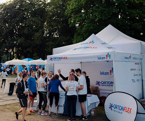 People gathered around an OrtonFlex promotional tent at an outdoor event with trees in the background.