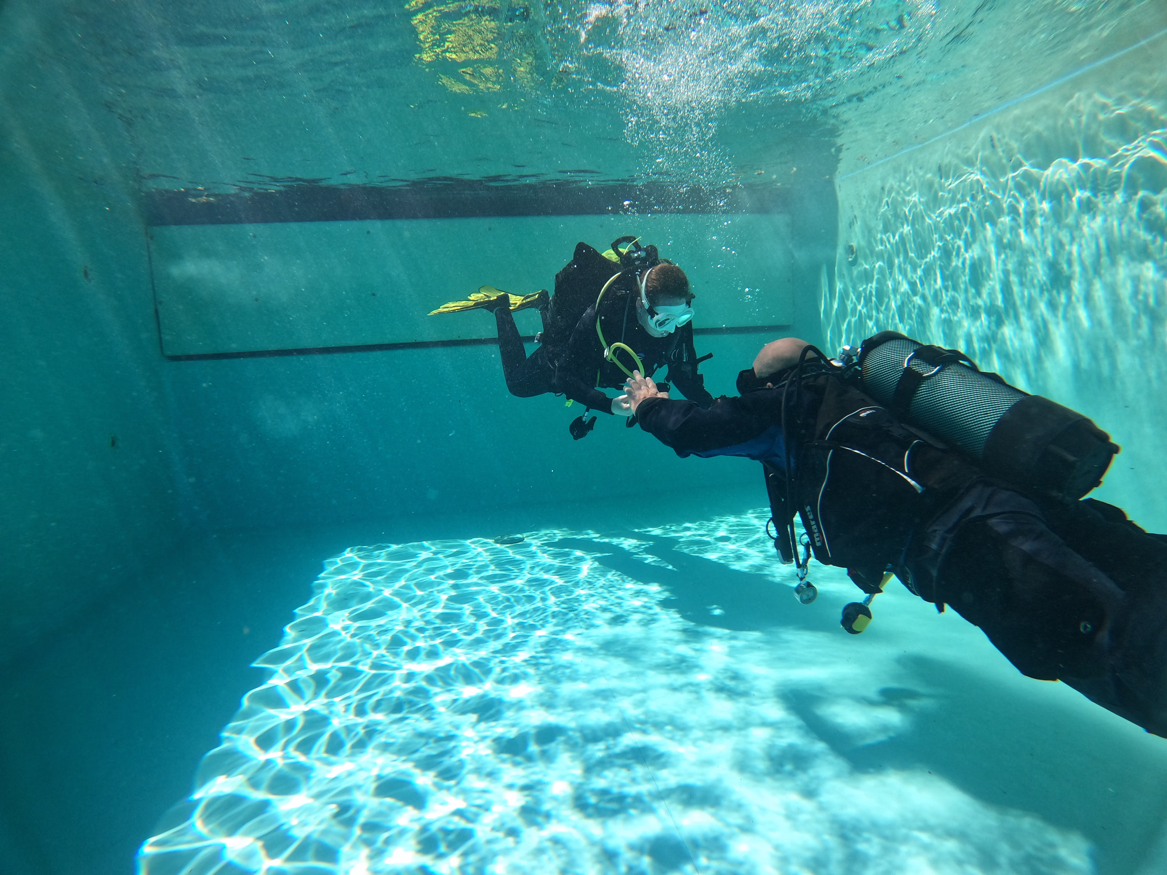 Duikers zitten onderwater in een zwembad en trainen de lichaamshouding, trim.