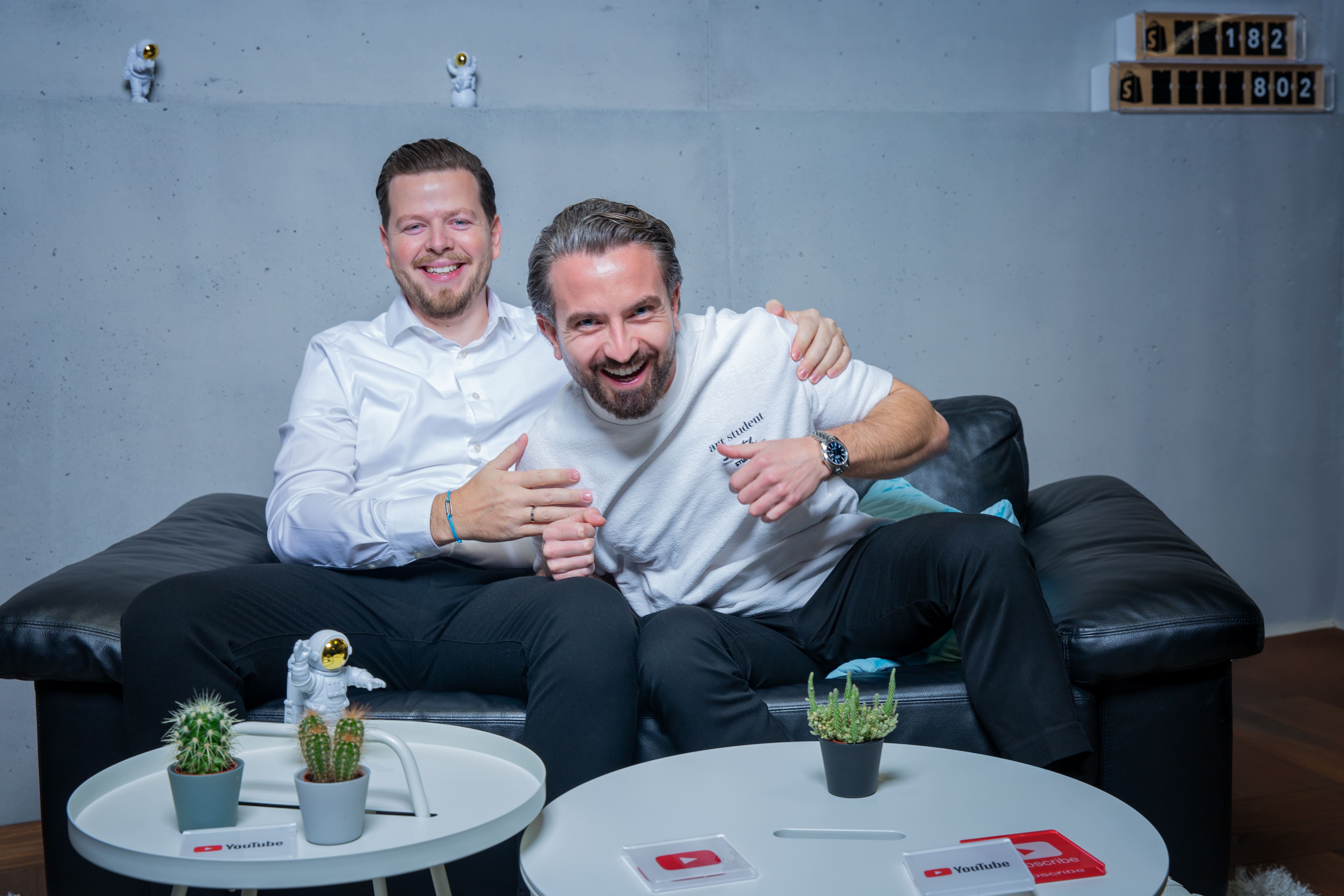 Moreno Carroccia & Flamur Sacipi lachend auf einem Sofa - Online Marketing Agentur Südostschweiz & Liechtenstein (Chur, Landquart, Sargans, Buchs, Rheintal, Vaduz)