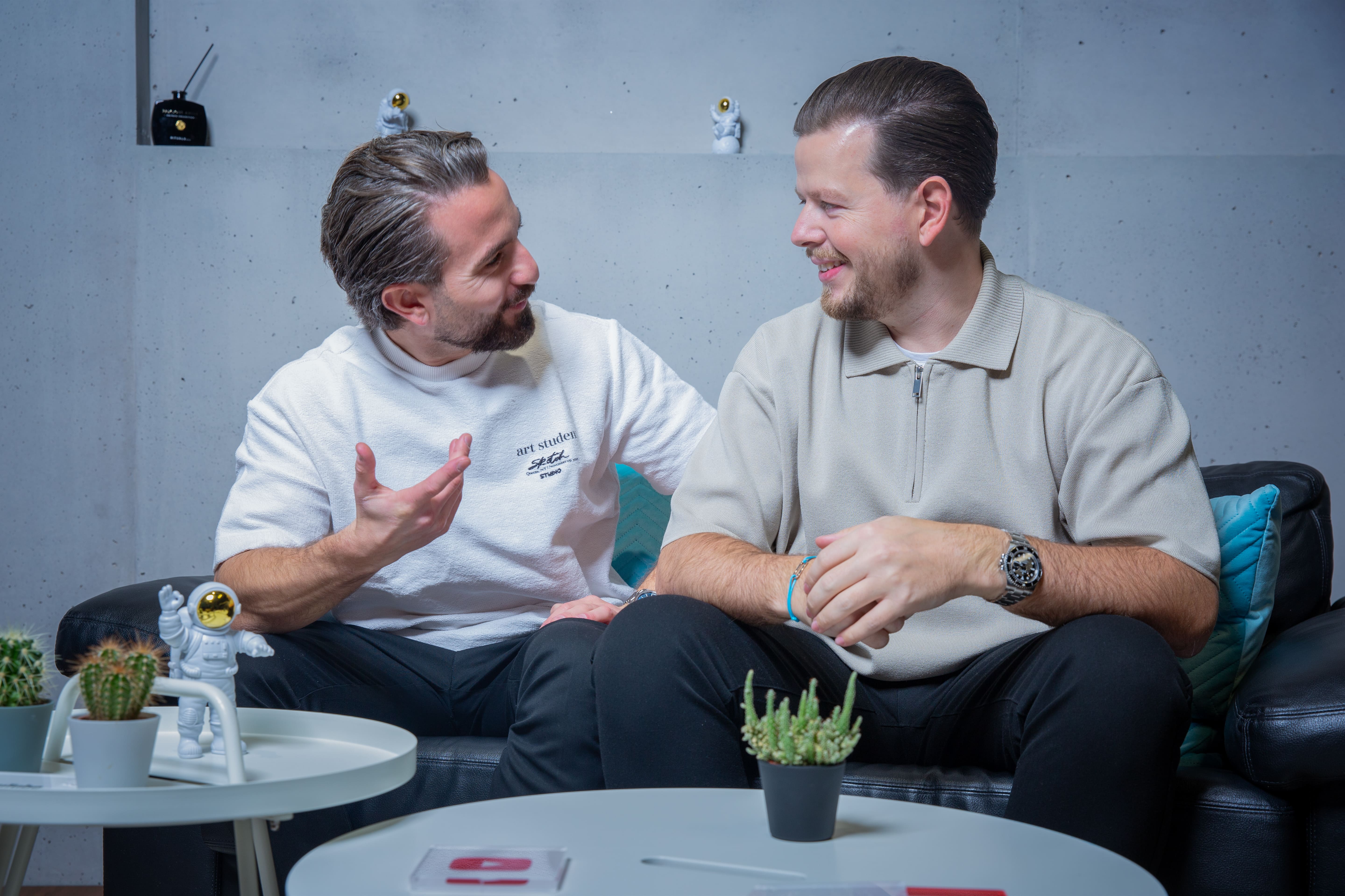 Moreno Carroccia & Flamur Sacipi auf einem Sofa und diskutieren lachend - Online Marketing Agentur Südostschweiz & Liechtenstein (Chur, Landquart, Sargans, Buchs, Rheintal, Vaduz)