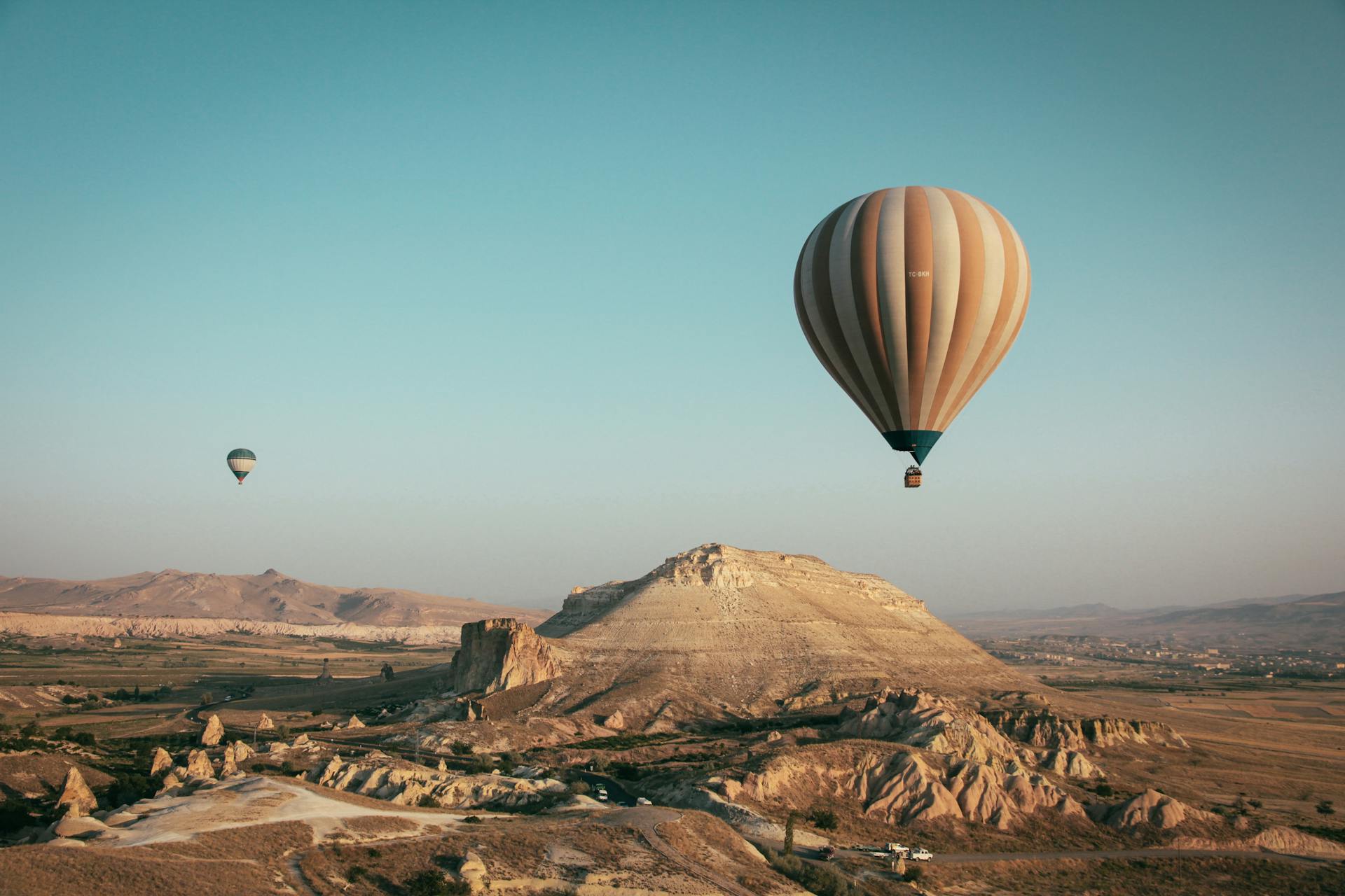 Two hot air balloons floating over a rocky, desert landscape with a clear blue sky.