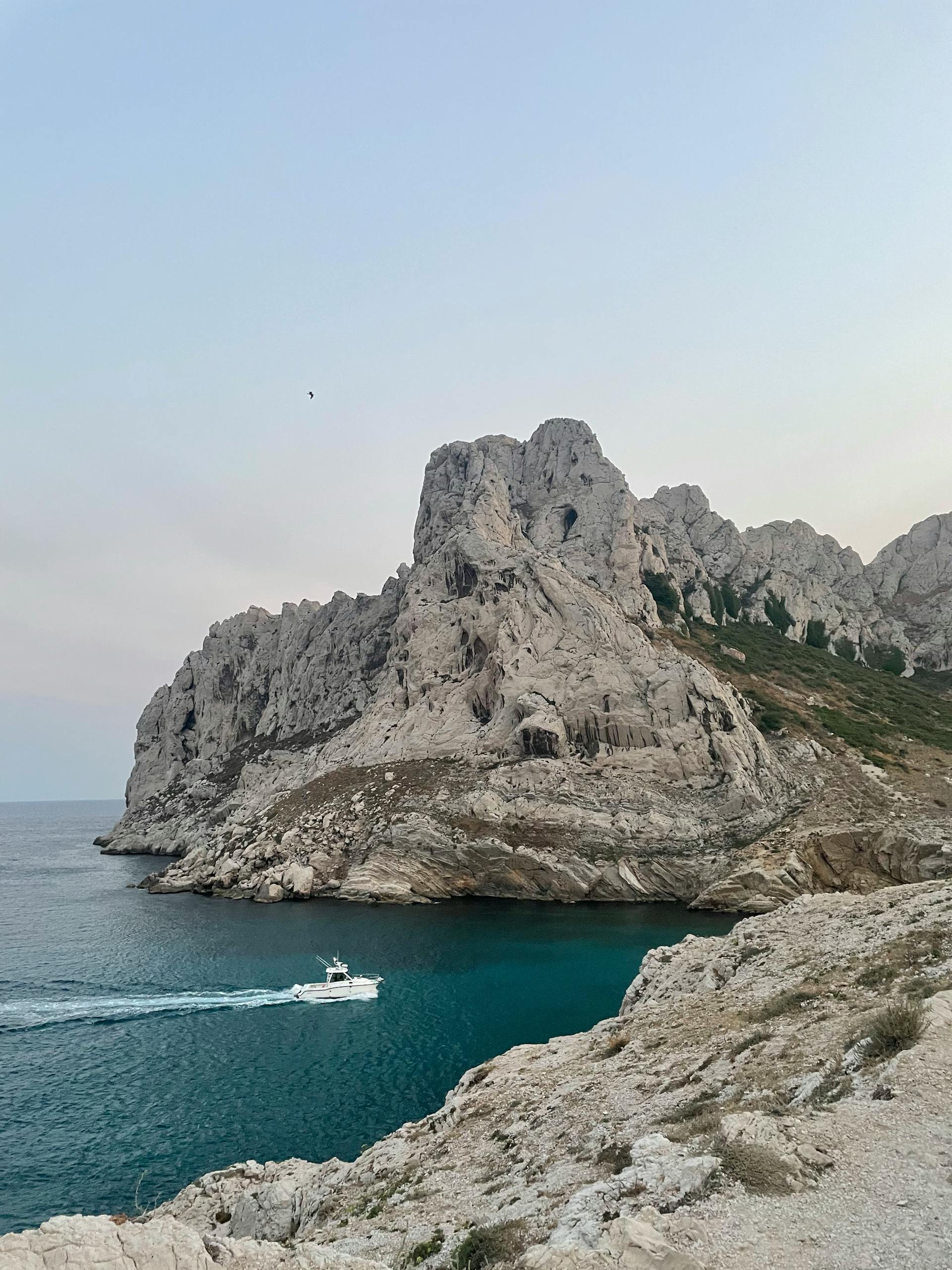 White motorboat cruising through deep blue water near a rocky cliff with sparse vegetation under a clear sky.