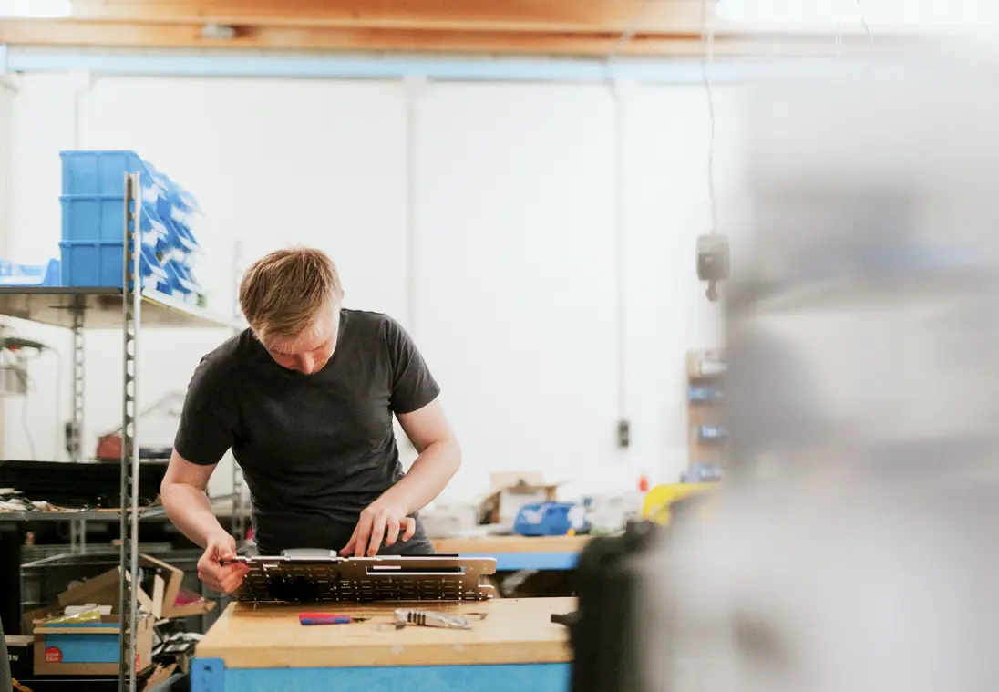 Man werkt geconcentreerd aan een elektronisch apparaat op een werkbank in een werkplaats.