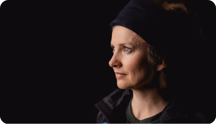 Profile of a woman wearing a dark headband and jacket looking thoughtfully to the right against a black background.