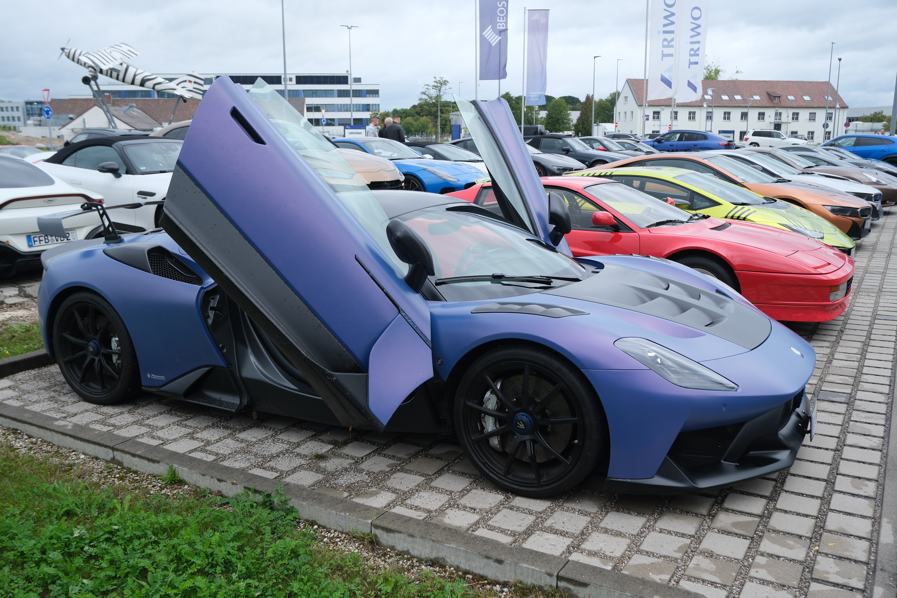 Eine Reihe an bunten, hochperformanten und hochpreisigen Sportwägen, die auf einem Parkplatz stehen im Rahmen einer Ausfahrt.