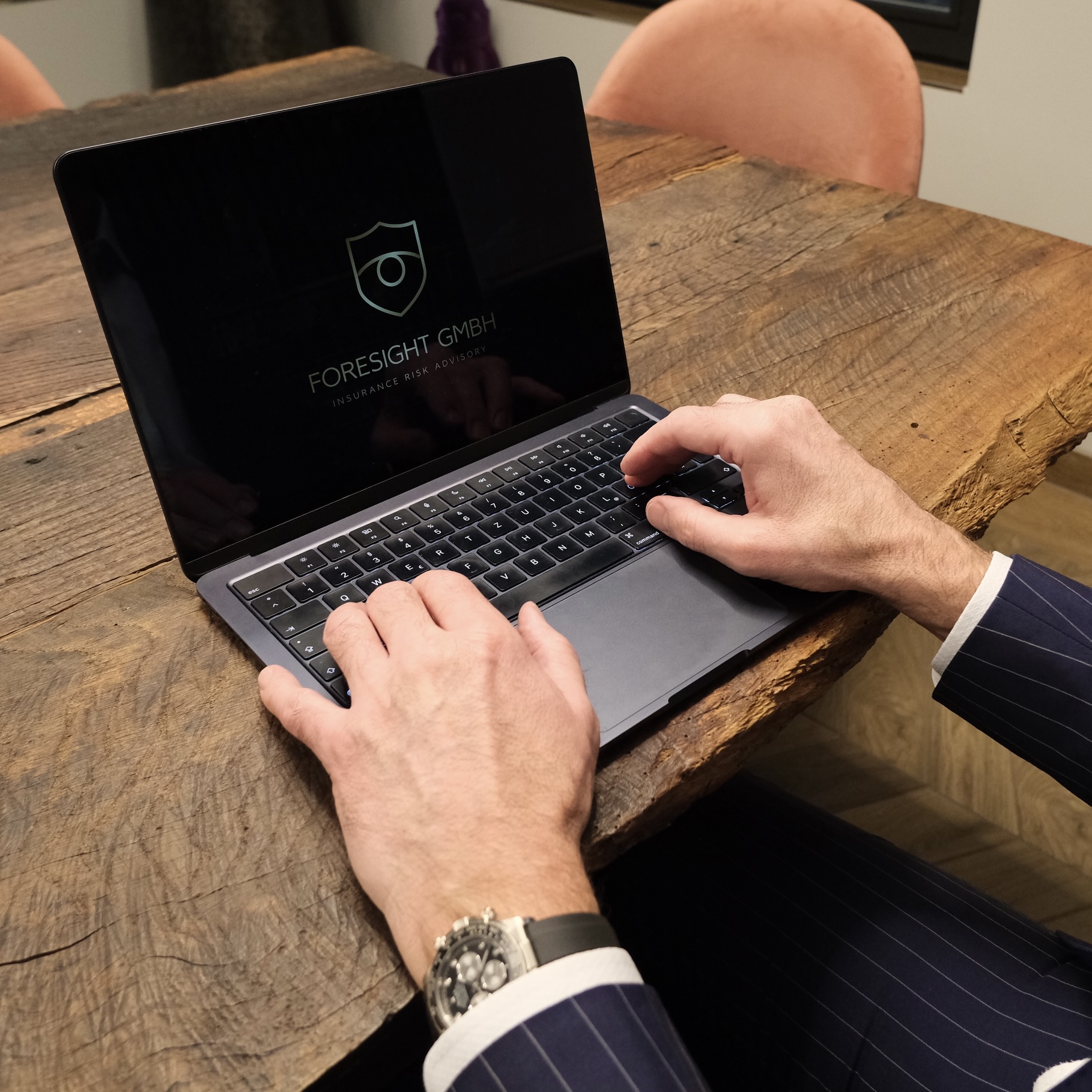 Ein Mann sitzt an einem Holztisch und hat seine Hände auf der Tastatur eines Laptops, auf dessen Bildschirm man das Logo der Firma erkennen kann.