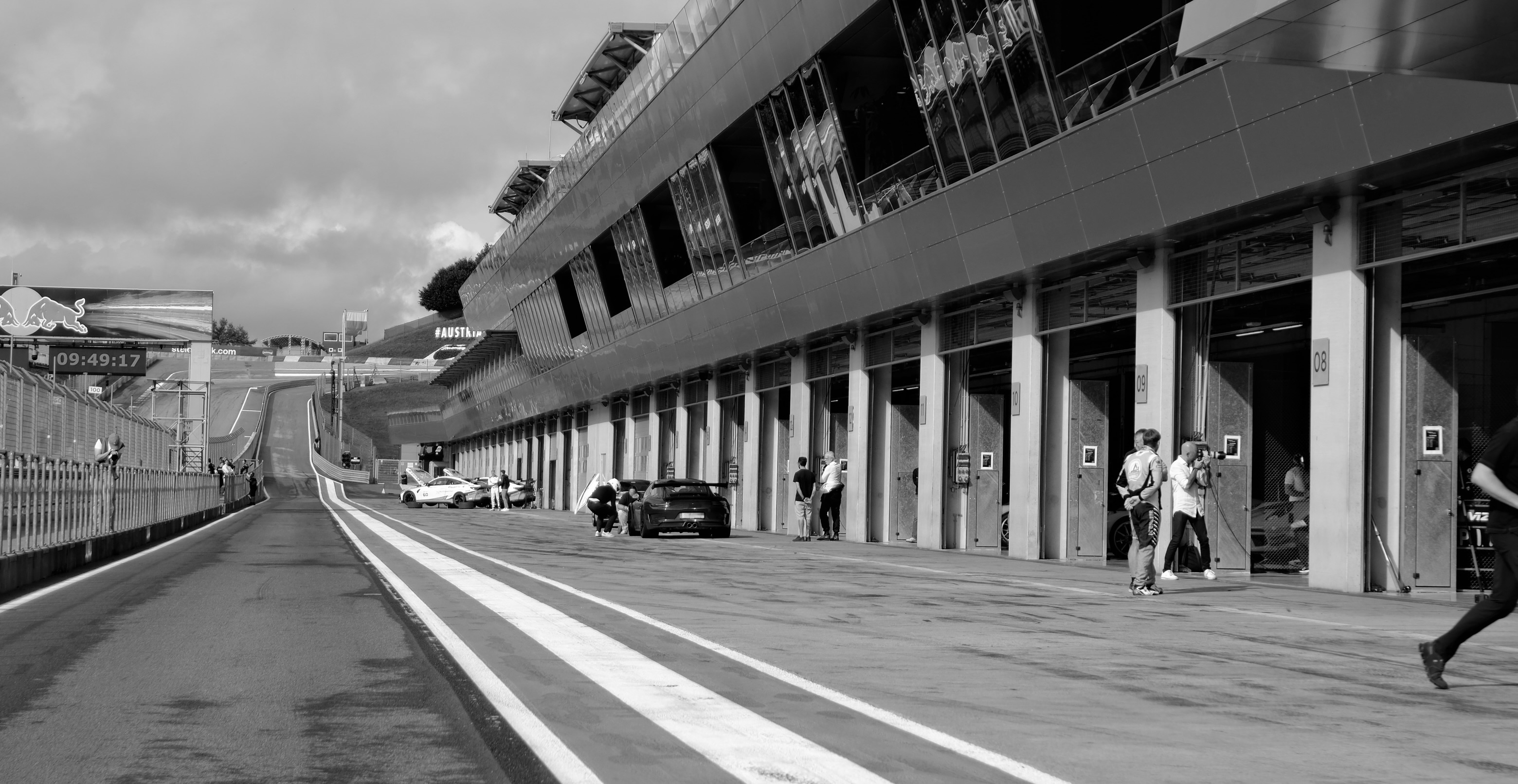 Blick von der Boxengasse aus zu den einzelnen Boxen. Das Bild ist schwarz-weiß. In der Ferne sieht man einzelne Sportwägen.