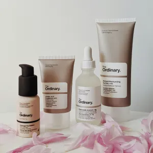 assortment of light brown bottles and tubes of skincare product surrounded by pink petals