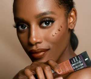 Dark skin woman with long eyelashes looking at camera holding a skincare product