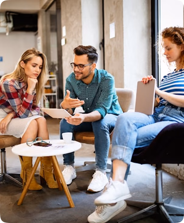 Trois jeunes adultes assis dans un bureau moderne discutent en regardant une tablette.