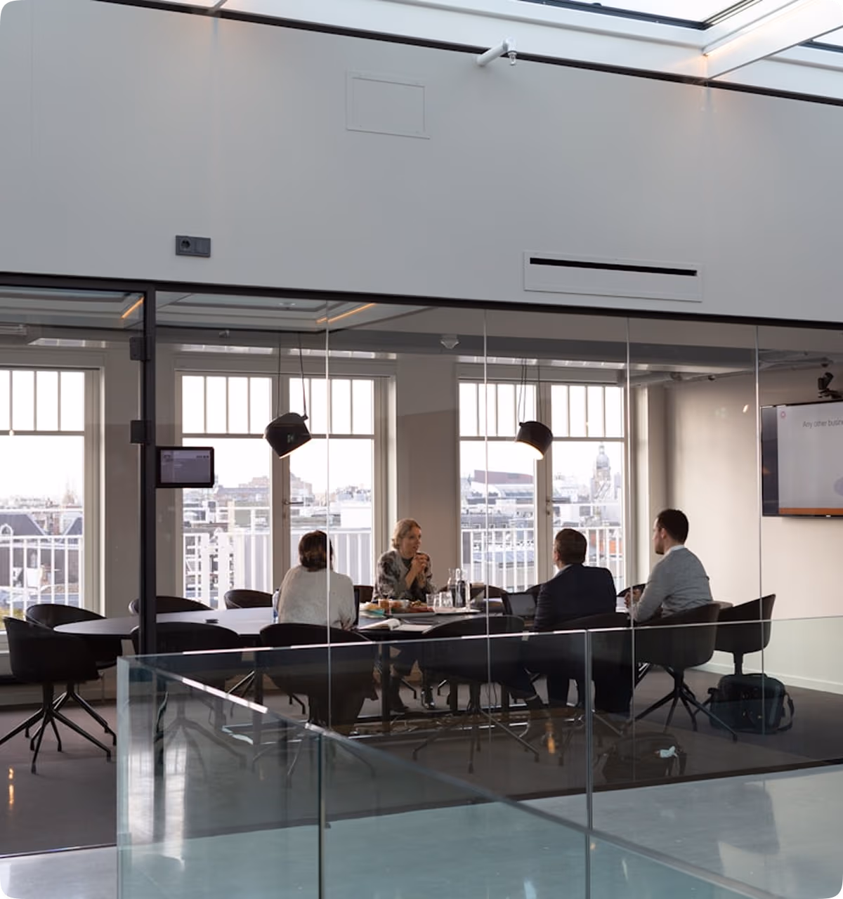 Quatre personnes en réunion autour d'une table dans une salle de conférence avec grandes fenêtres et vue sur la ville.