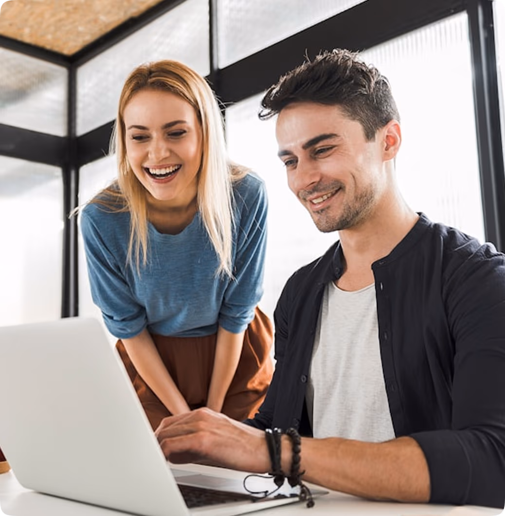 Deux collègues souriants regardant un ordinateur portable dans un bureau lumineux.