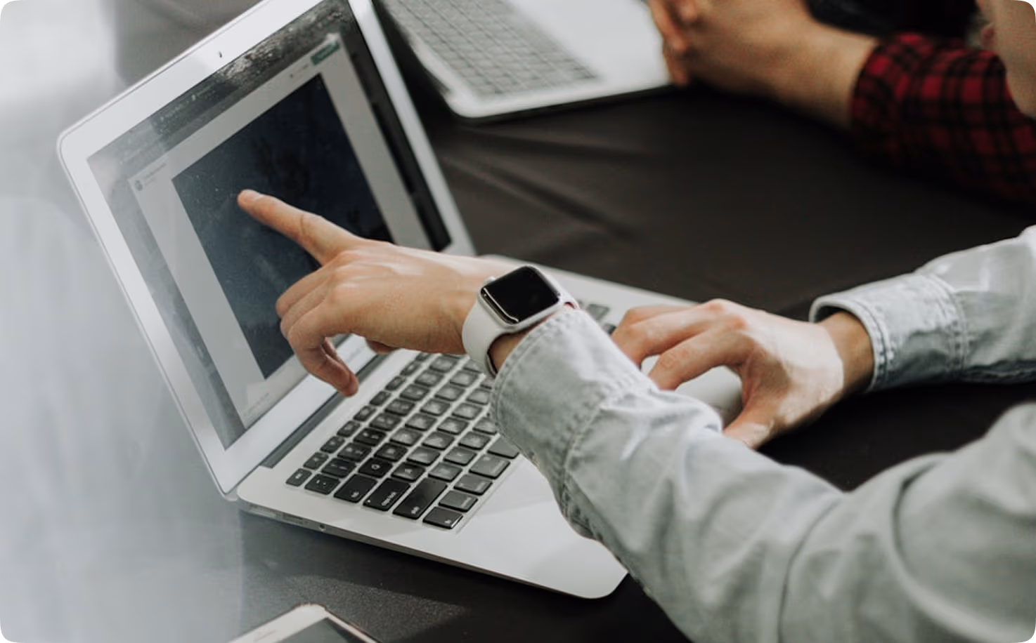 Une personne portant une montre connectée pointe l'écran d'un ordinateur portable.