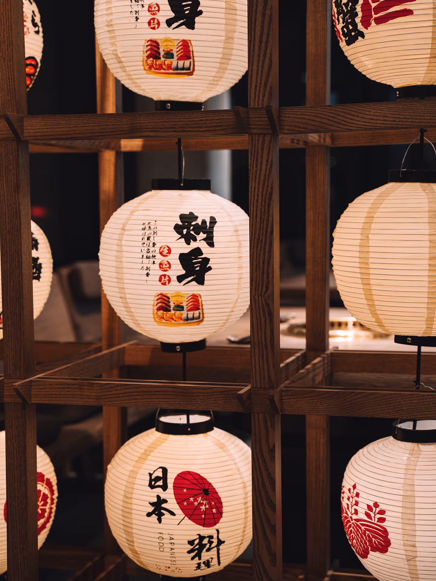 White Japanese paper lanterns with black and red kanji characters hanging on a wooden frame.