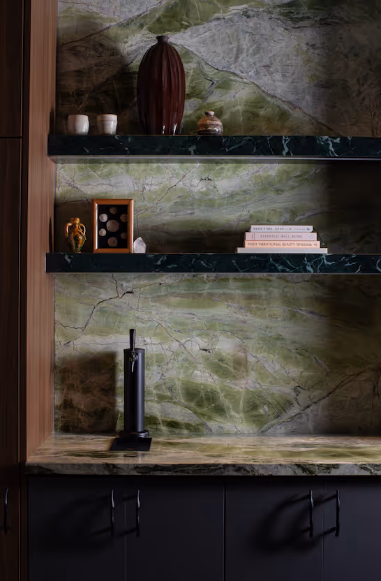 Kitchen area with green marble backsplash and shelves holding decorative items and books, and a coffee machine on the countertop.