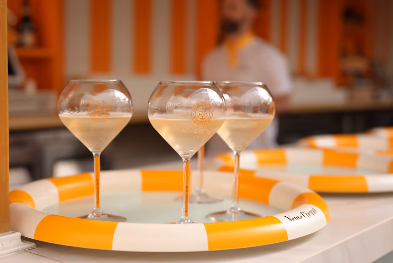 Three glasses of Veuve Clicquot champagne on an orange and white striped serving tray with a blurred background.