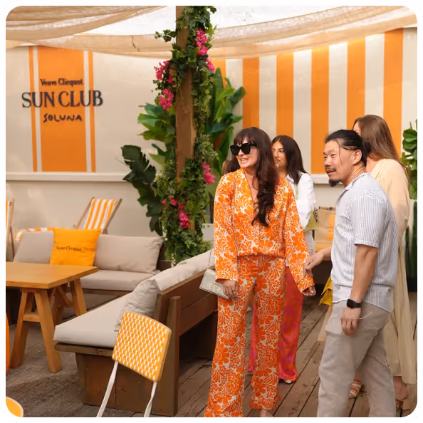 Four people socializing in a stylish outdoor lounge area with orange and white decor labeled Veuve Clicquot Sun Club Soluna.