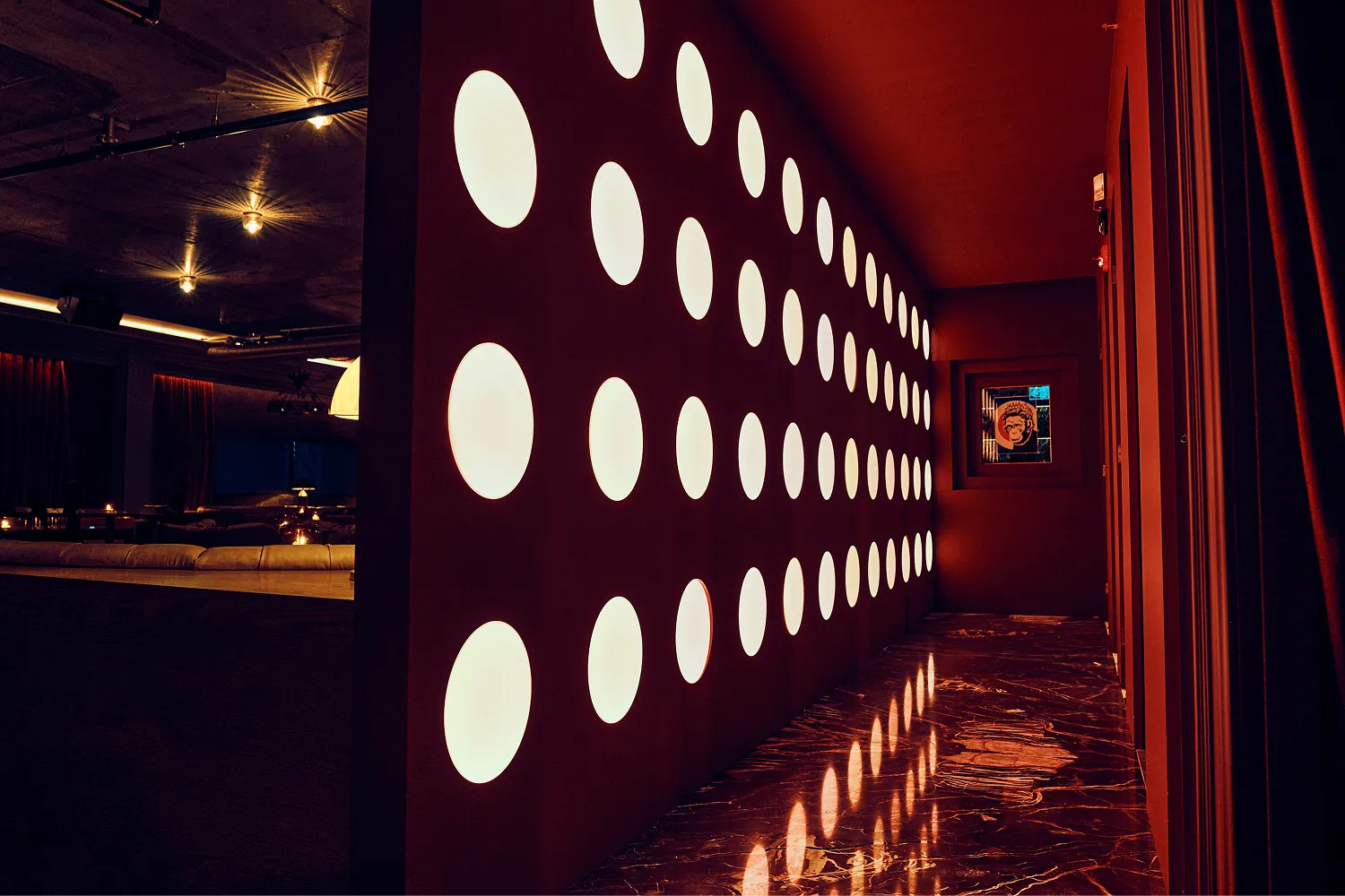 Dimly lit modern hallway with a wall featuring evenly spaced circular lights and a polished marble floor reflecting them.