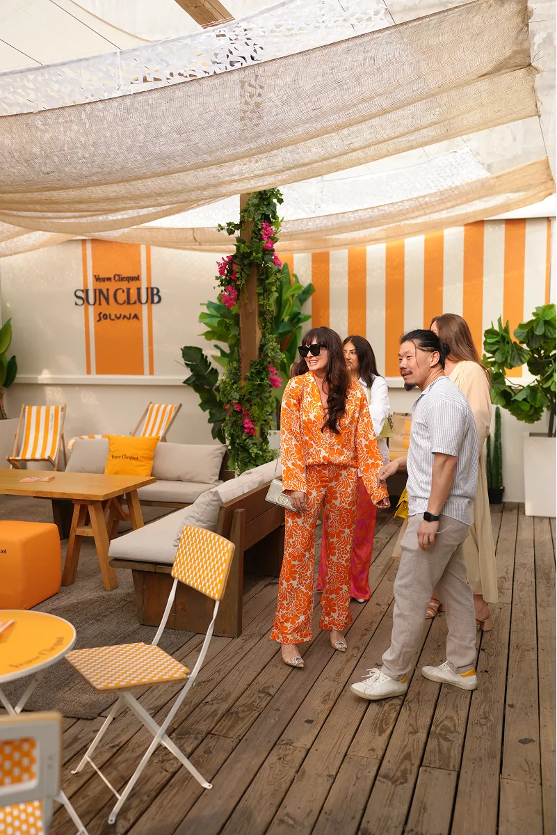 Group of four people socializing at Veuve Clicquot Sun Club Soluna with orange and white striped decor and wooden flooring.