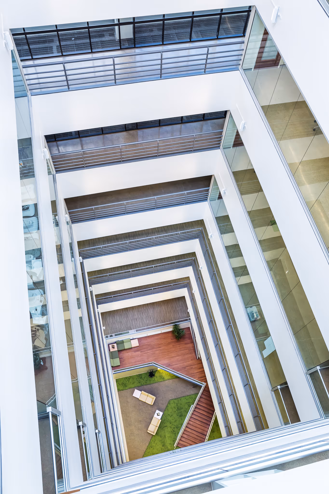 Top-down view of a modern multi-story atrium with glass walls, railings, and seating area at the bottom.