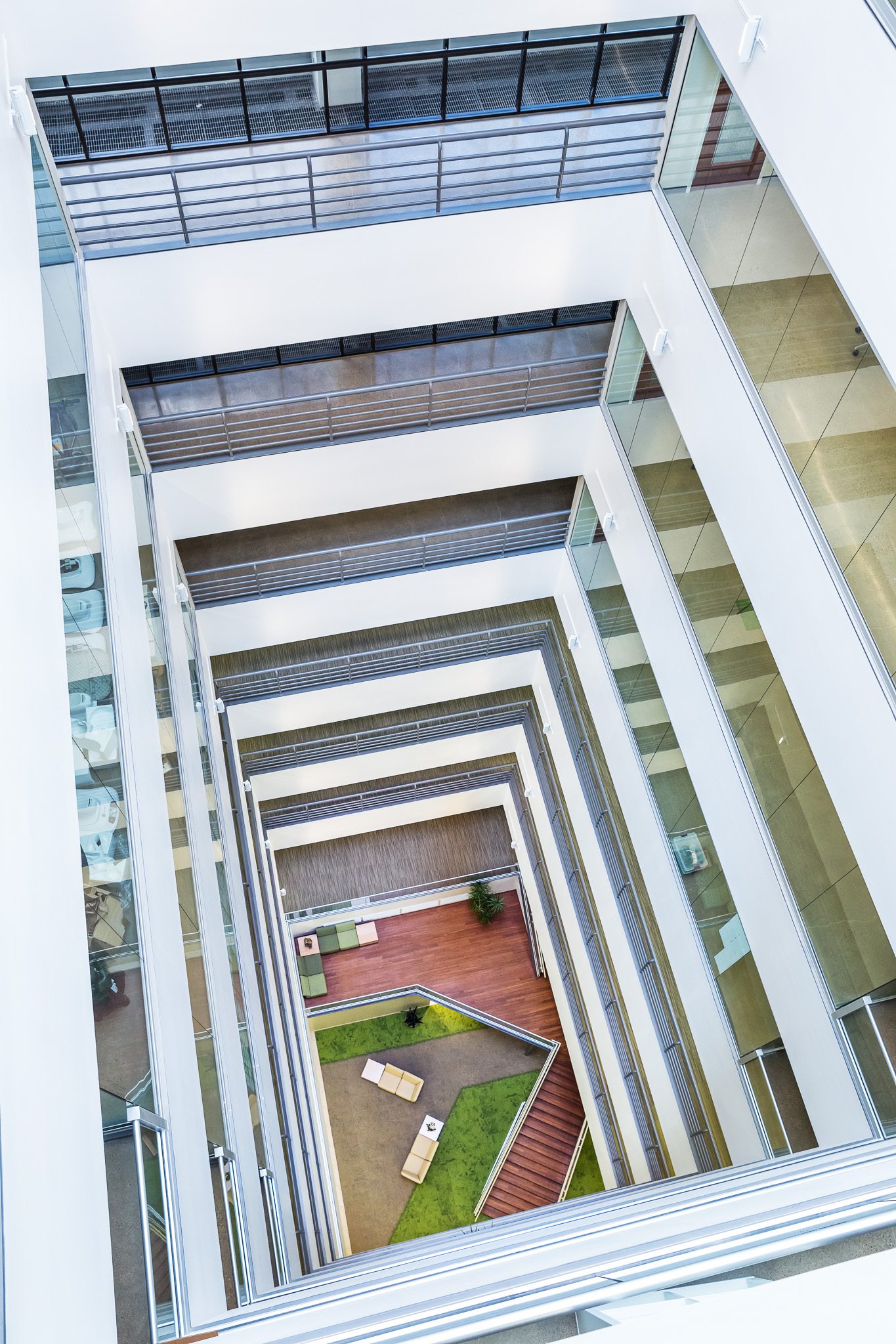 Top-down view of a modern multi-story atrium with glass walls, railings, and seating area at the bottom.