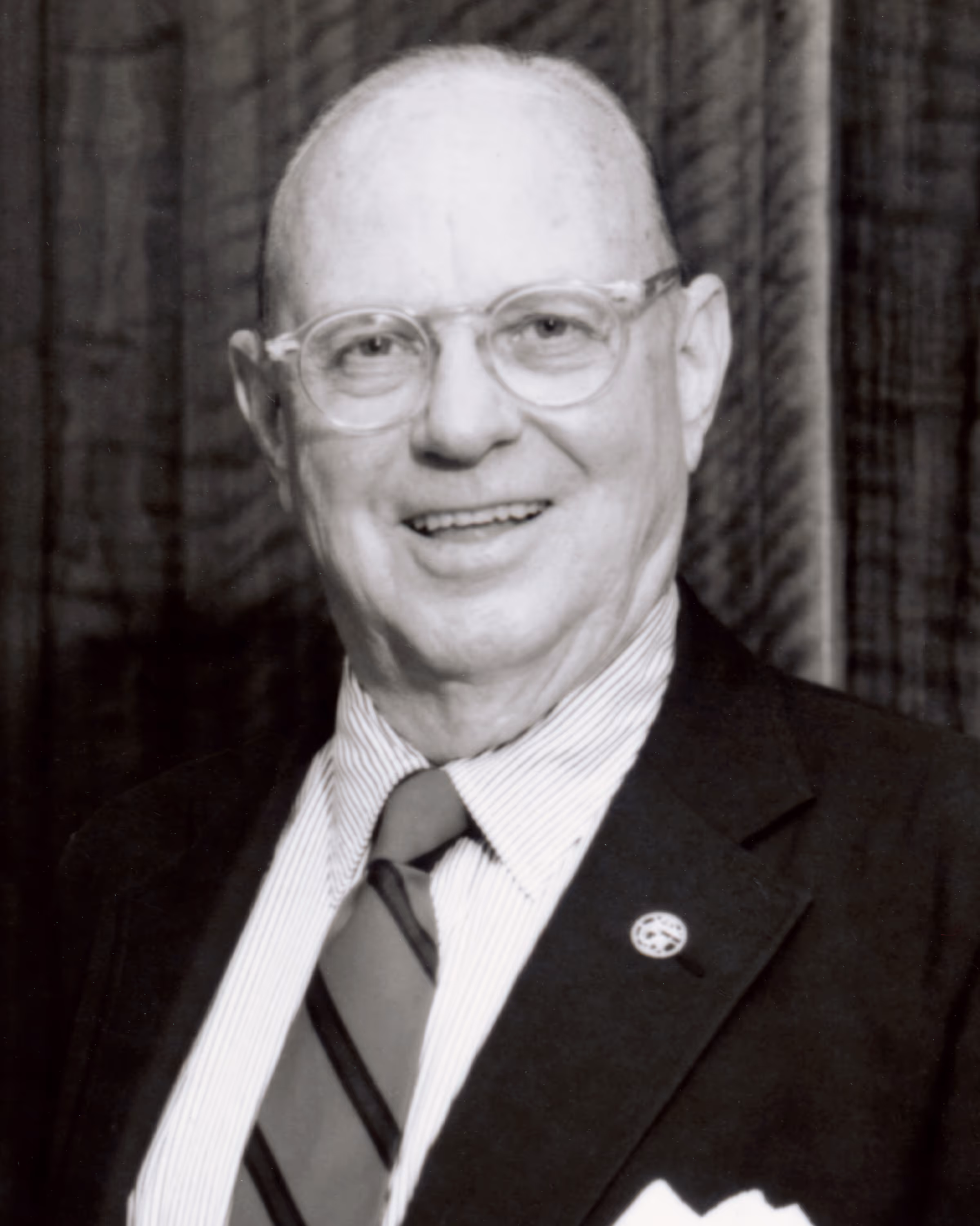 Portrait of a smiling elderly man with glasses wearing a suit jacket, striped shirt, and striped tie.