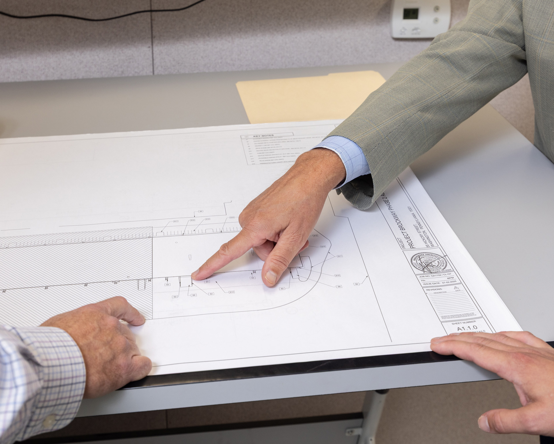 Hands of three people pointing at a detailed architectural blueprint on a desk.