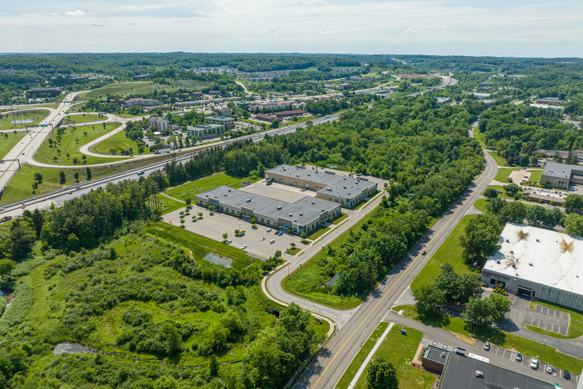 Aerial view of an industrial complex surrounded by green trees and fields, with nearby highways and roads.