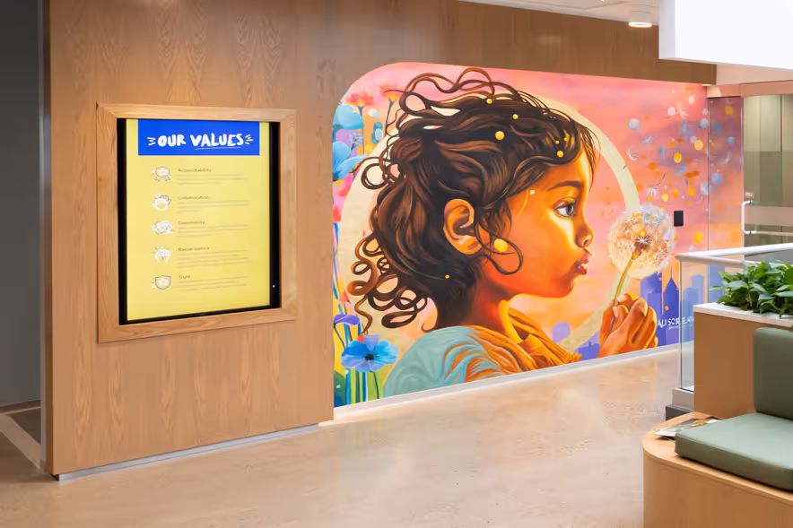 Mural of a young girl with curly hair blowing dandelion seeds, next to a wall display titled 'Our Values' inside a modern building.