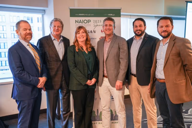 Six professionally dressed individuals standing indoors in front of a NAIOP 2025 banner in a conference setting.