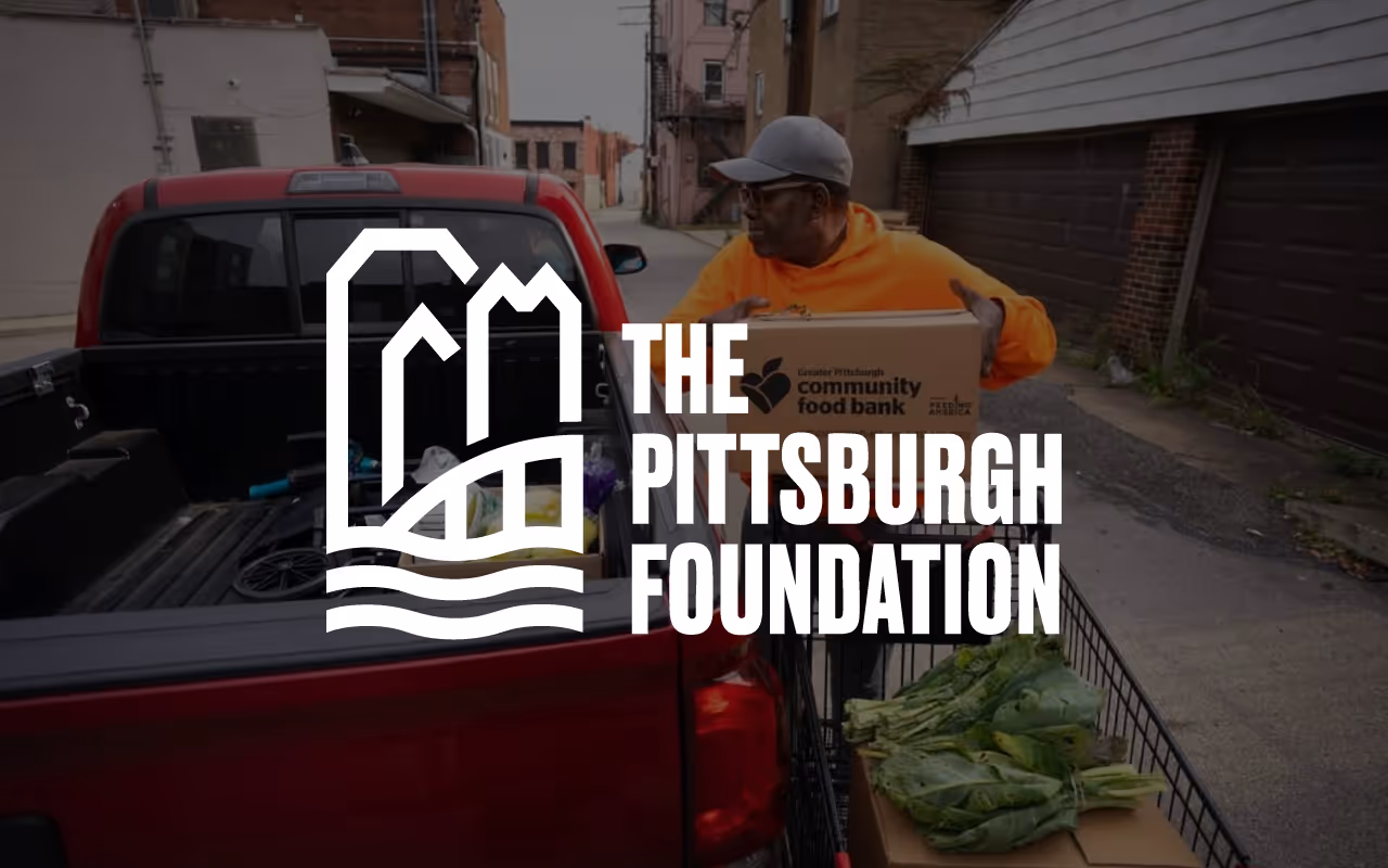 Man in orange hoodie loading boxes into a red pickup truck next to a shopping cart with leafy greens, overlaid with The Pittsburgh Foundation logo.
