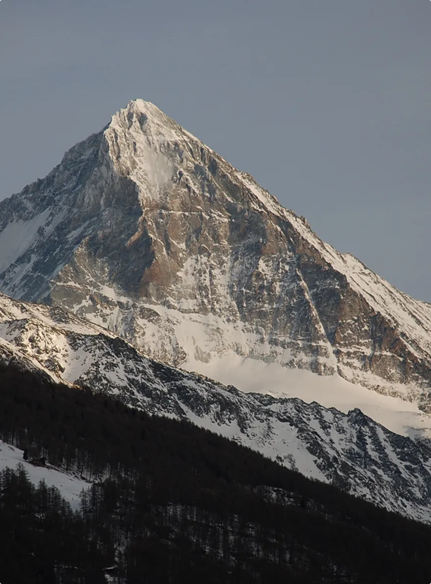 Snow-covered Dent Blanche mountain peak against a clear sky at sunset.