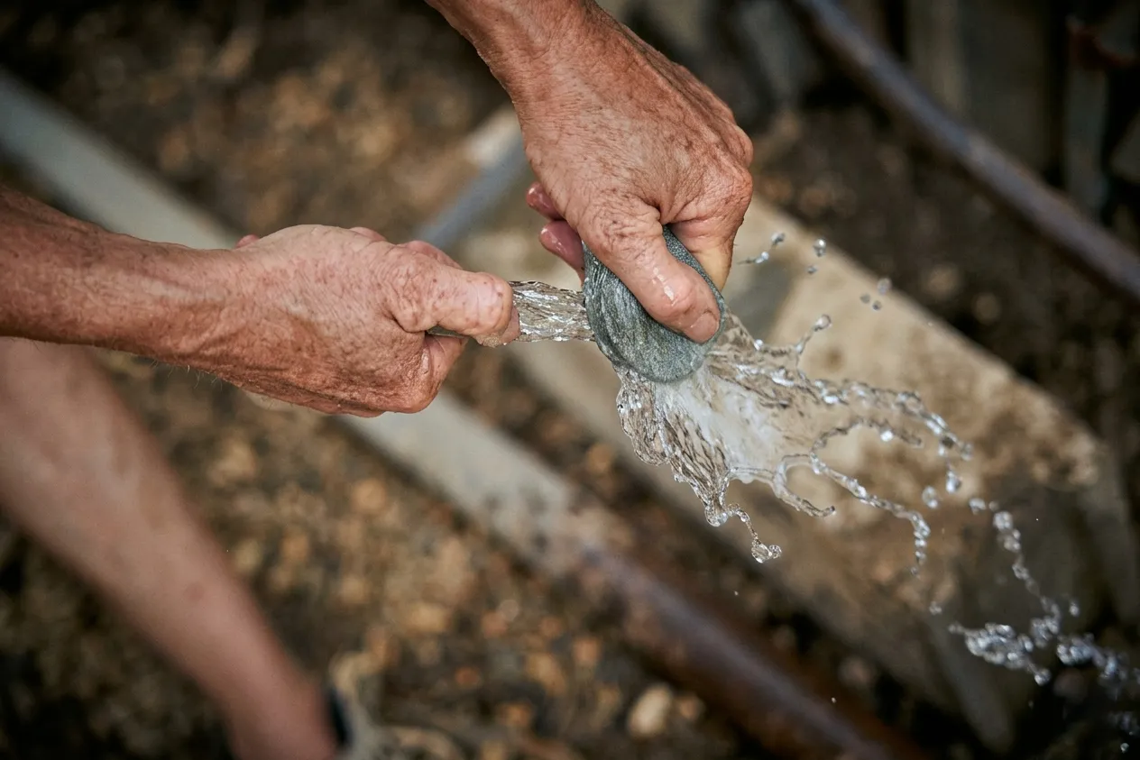 Close-up of two hands squeezing water from a wet rag or sponge outdoors.