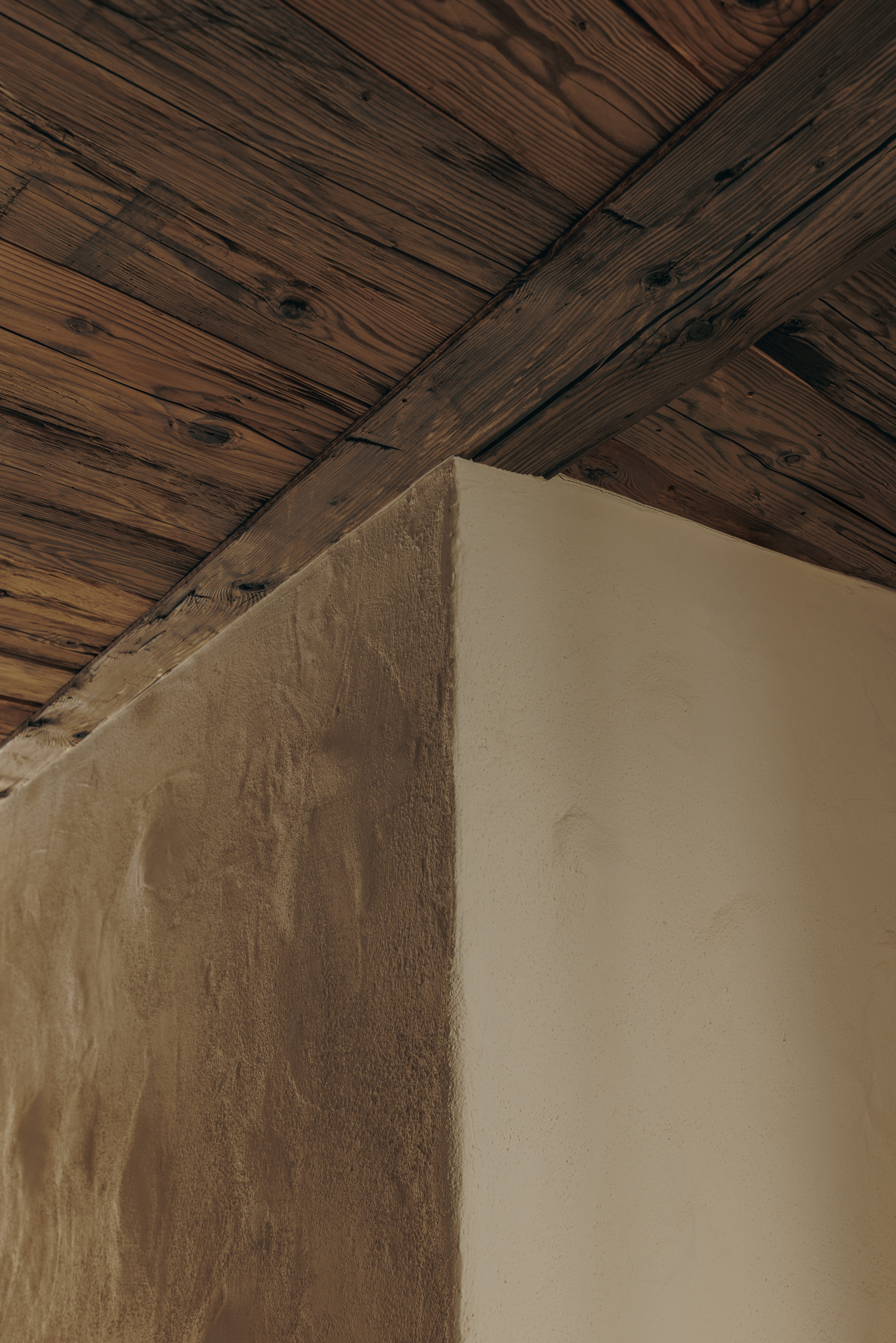 Corner of a textured beige wall meeting a wooden ceiling with visible knots and grain.