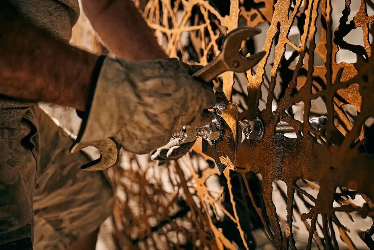Close-up of a person wearing work gloves using a wrench to tighten a bolt on a rusted metal gate with intricate cutout patterns.