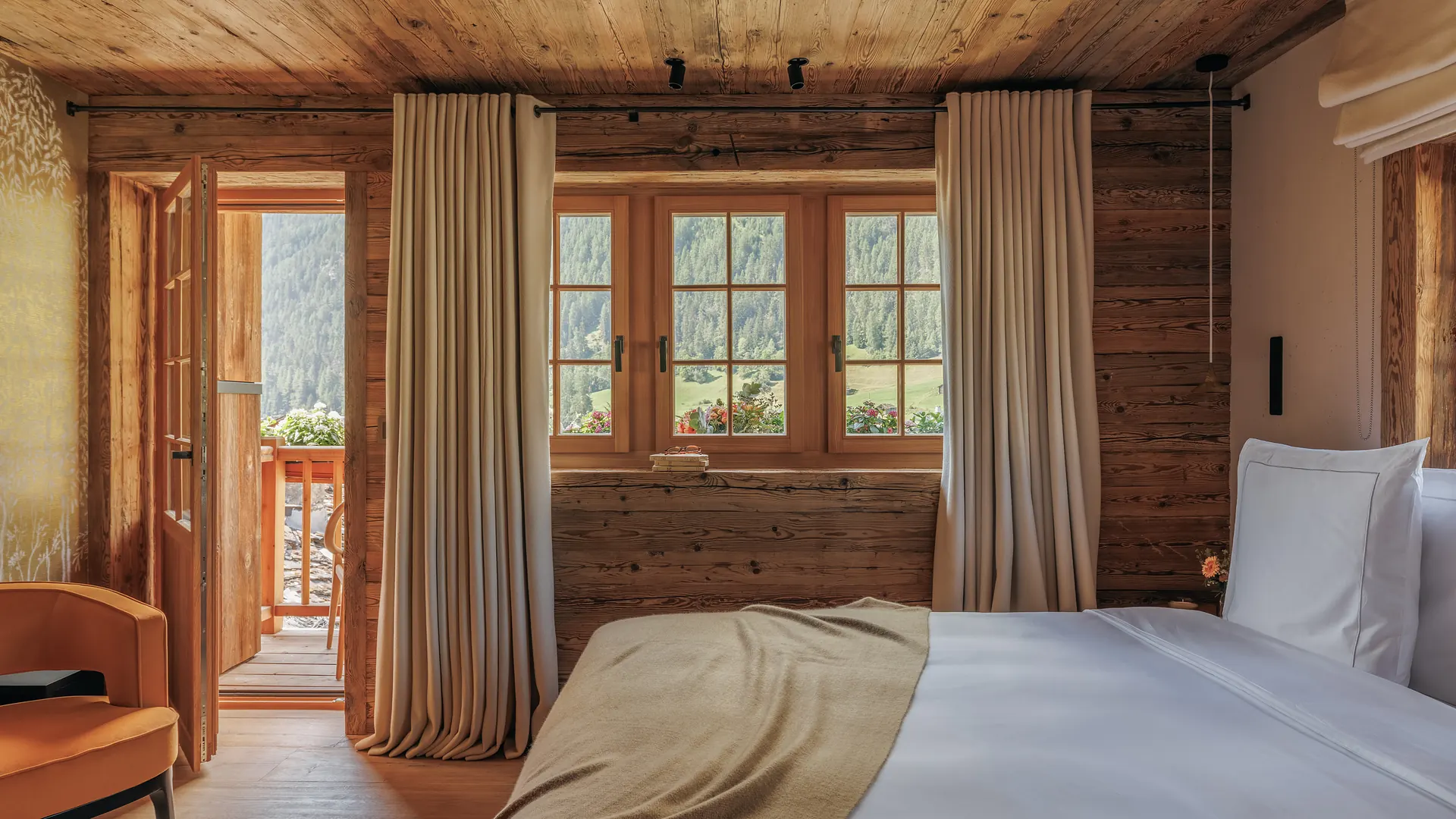 Chalet bedroom with a balcony door opening onto the valley and an orange armchair