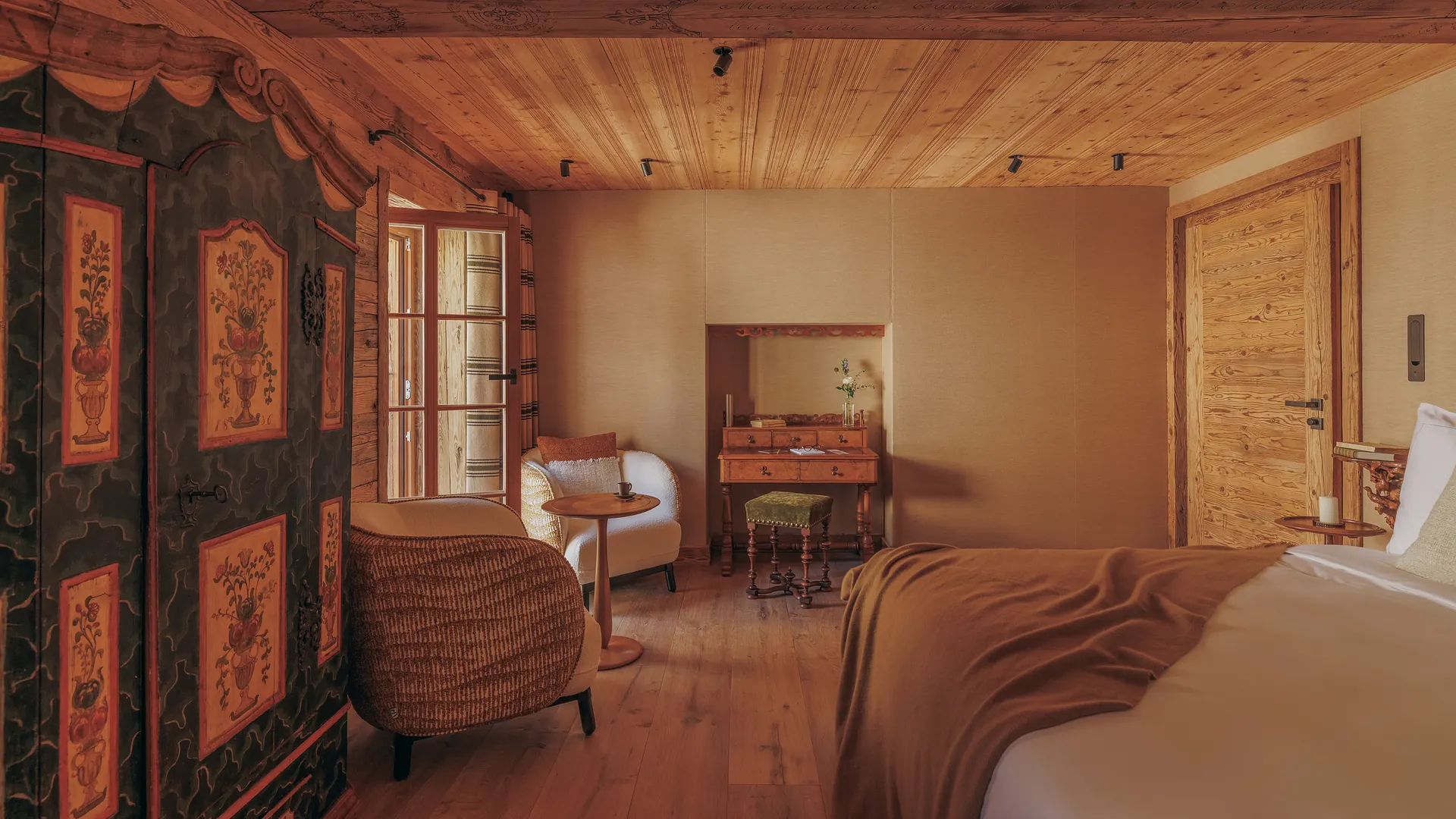 Full view of the Bochi room showing a painted folk-art wardrobe, armchairs, antique desk and bed with a camel throw