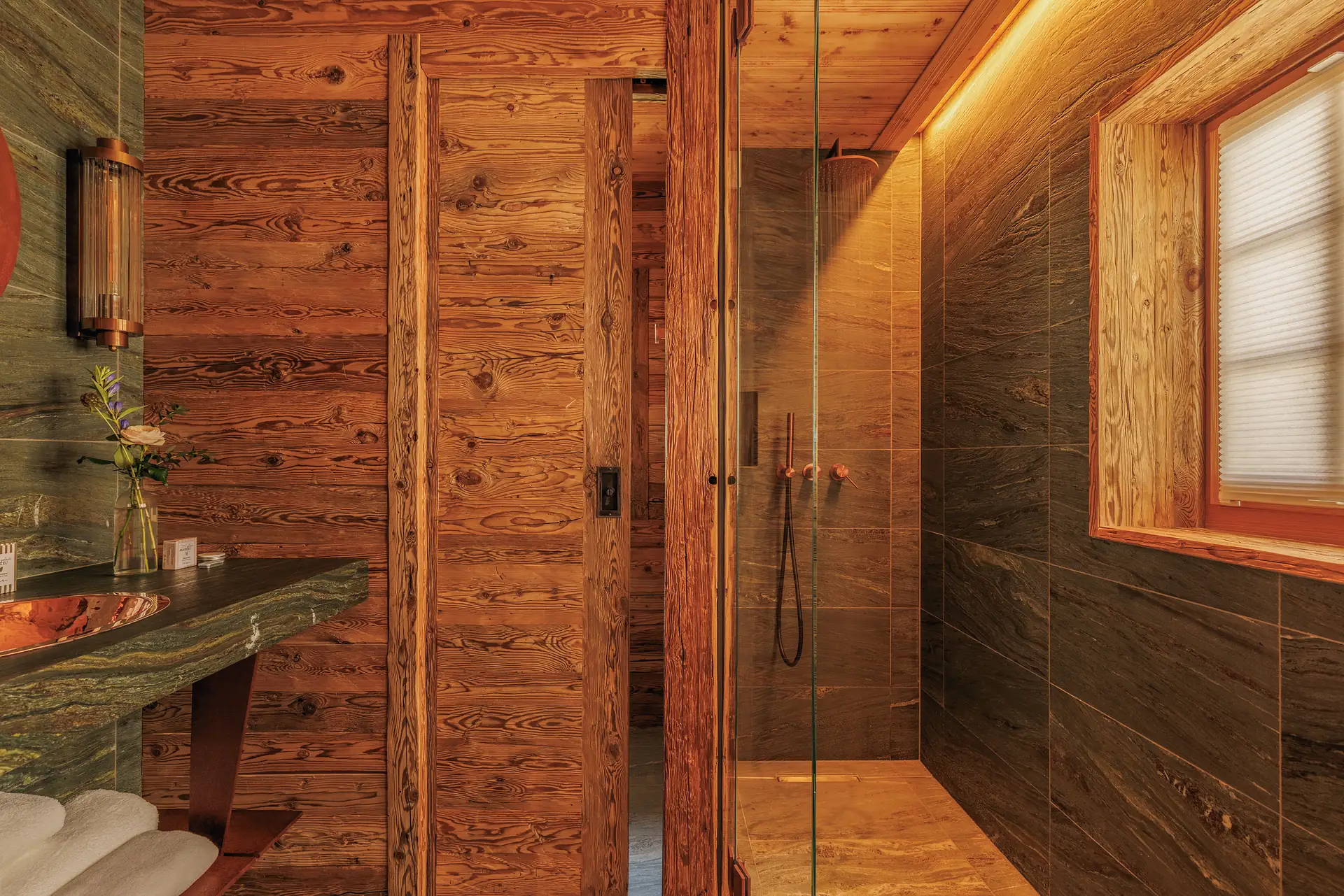 Bathroom with a green stone vanity, copper basin and a glass walk-in shower with a rainfall head and amber lighting