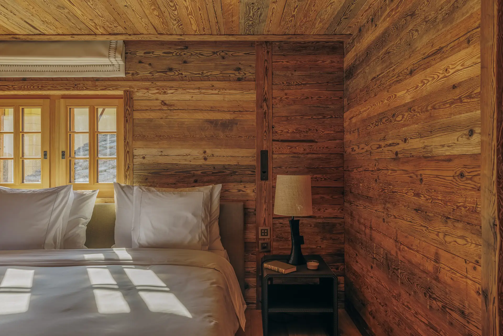 Wood-paneled bedroom with pillows lit by sunlight through French windows