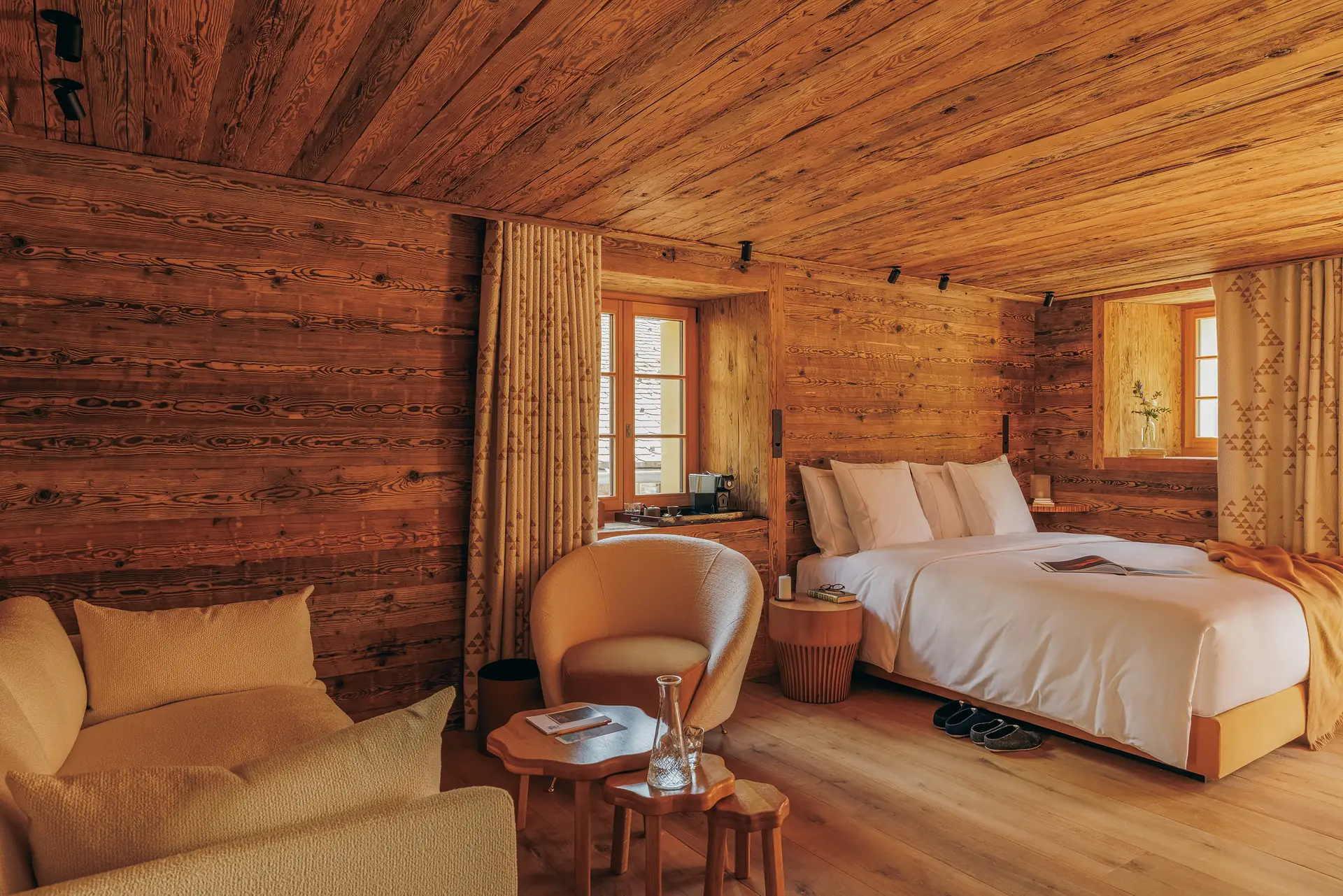 Cherra room overview with a double bed, caramel armchair, wood coffee table and two windows onto the village rooftops