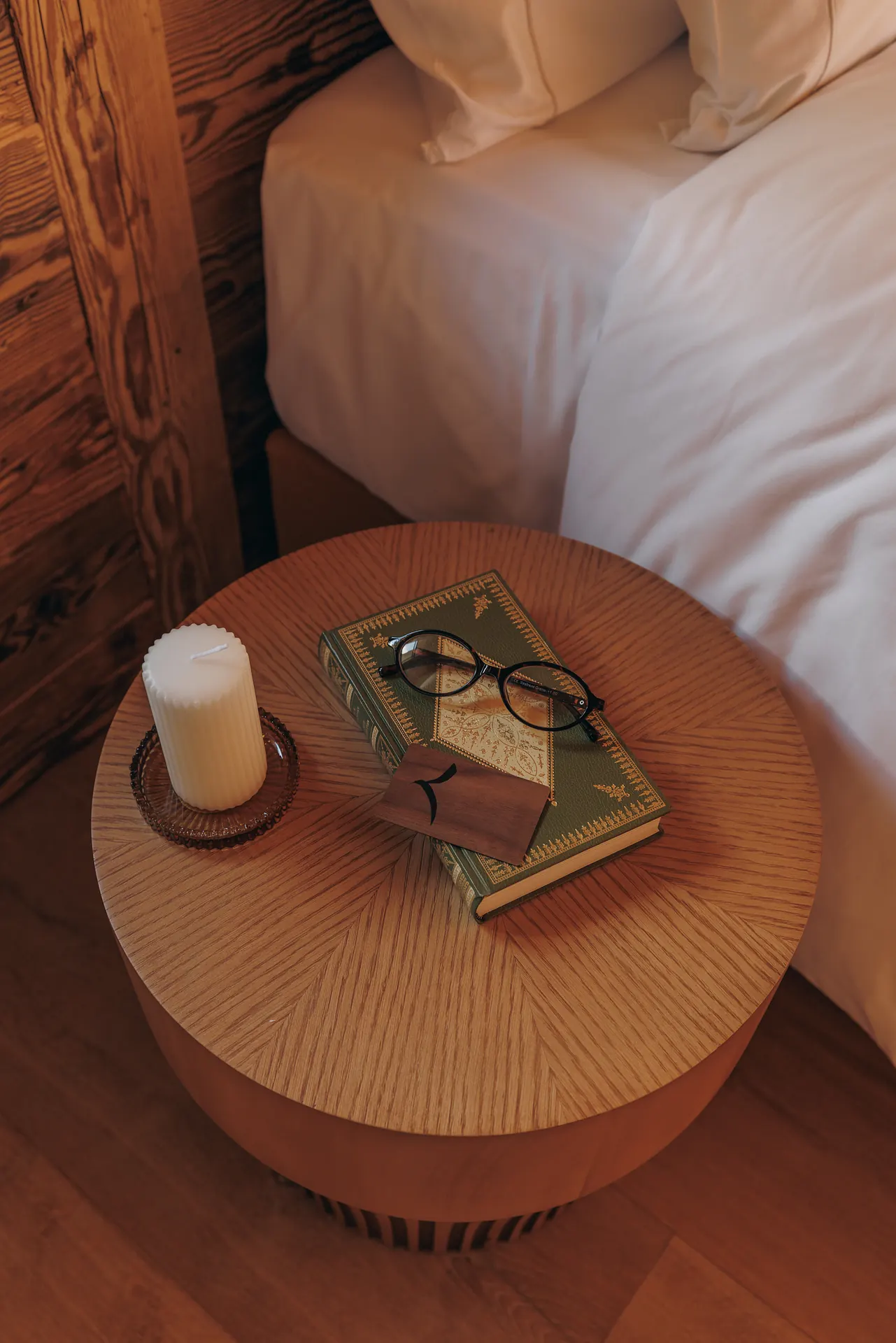 Runder Nachttisch aus gerippter Eiche mit einer Kerze, einem antiken Buch und einer Lesebrille neben dem Bett