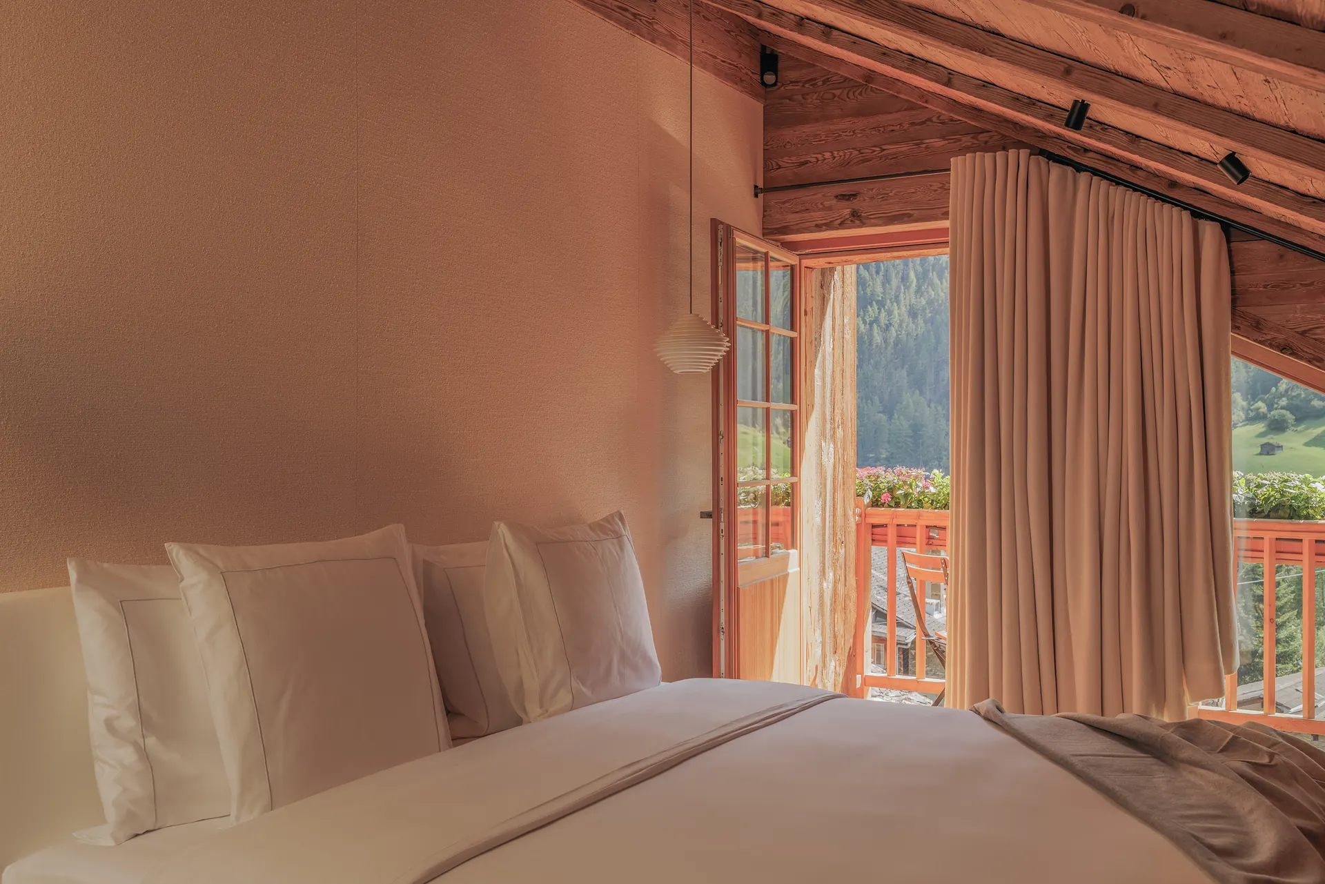 Double bed and ribbed pendant lamp in a terracotta-walled bedroom, balcony door open to pine forest and alpine meadows