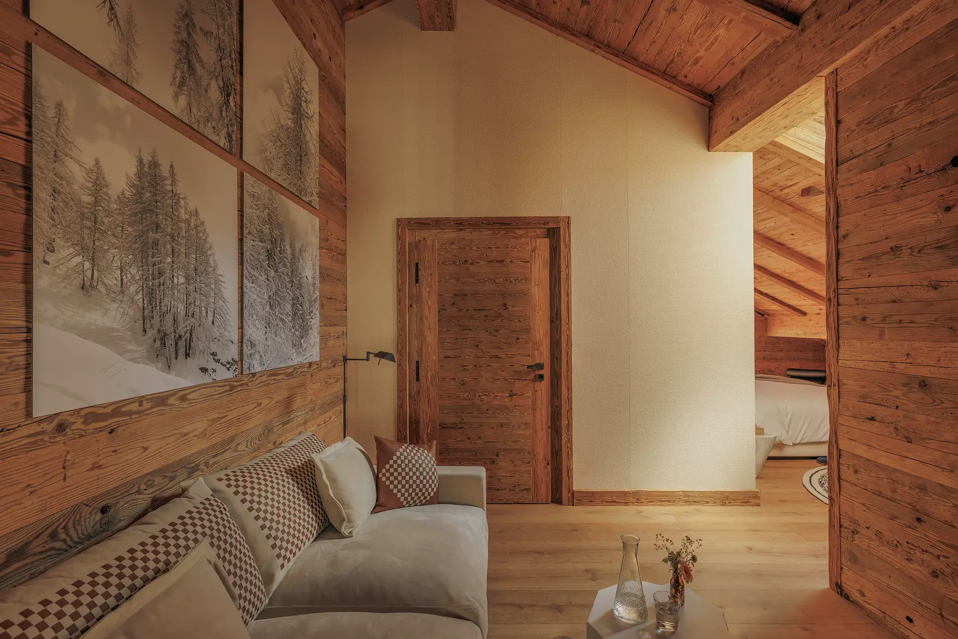 Suite with a high-pitched log ceiling, cream sofa, winter forest artwork and a doorway leading to the bedroom