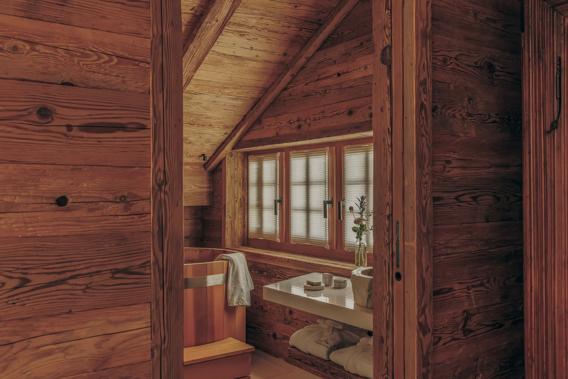 Attic bathroom seen through the doorway, with a cedar soaking tub, a window seat and bath amenities on a tray