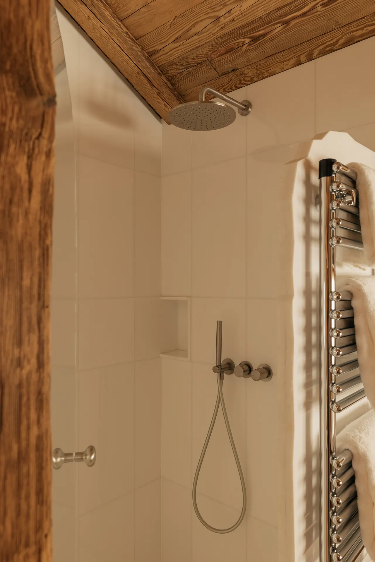 Minimal white-tiled shower with a round rainfall head, wall-mounted controls and a heated towel rail